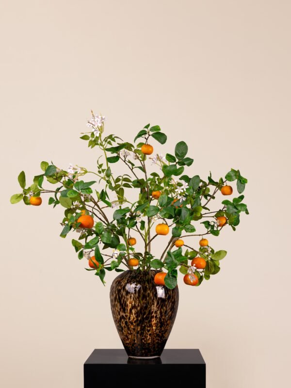 Faux orange spray arrangement with white blossoms and green leaves in a tall cheetah-patterned glass vase by Houz of Zen.