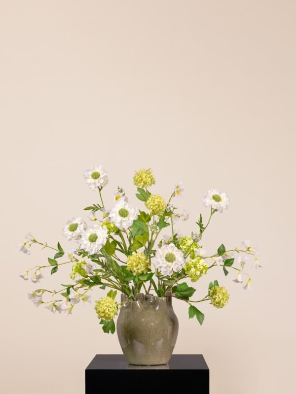 Faux green snowball, scabiosa, and campanula in a green ceramic vase on a black plinth