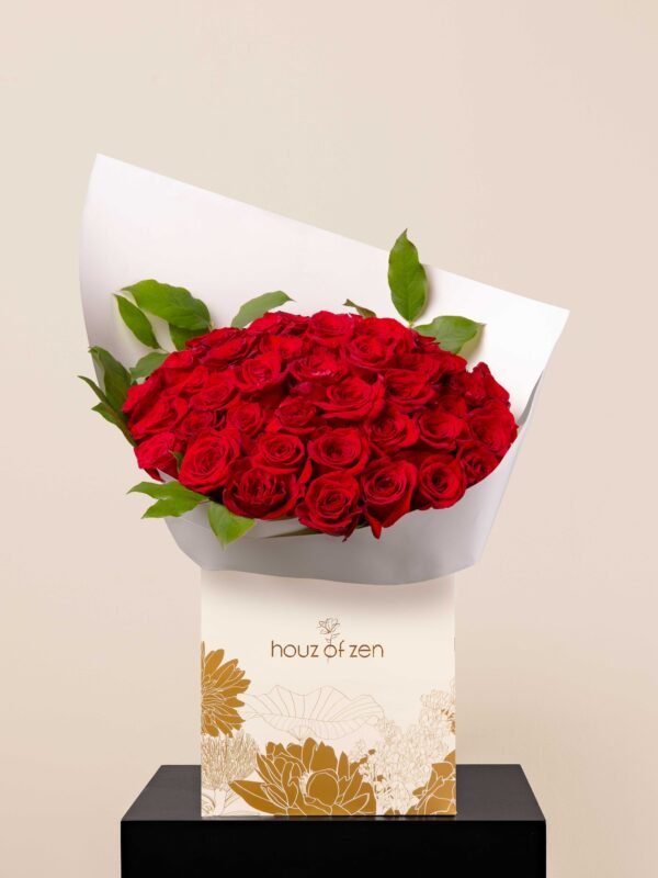 Opulent red rose bouquet wrapped in white paper with green foliage
