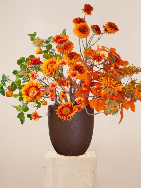 Artificial orange flower arrangement in Dubai with sunflowers, sprays, and autumn foliage in a brown vase.