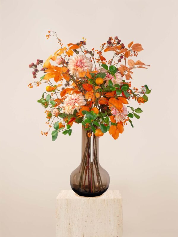 Artificial fall flower arrangement in Dubai with orange dahlias, peach blooms, berries, and autumn foliage in a tall glass vase.