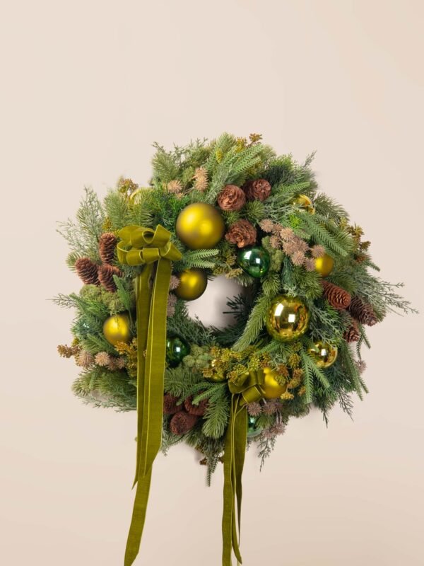 Olive green holiday wreath with faux pine foliage, pinecones, glossy green ornaments, and long olive velvet ribbons.